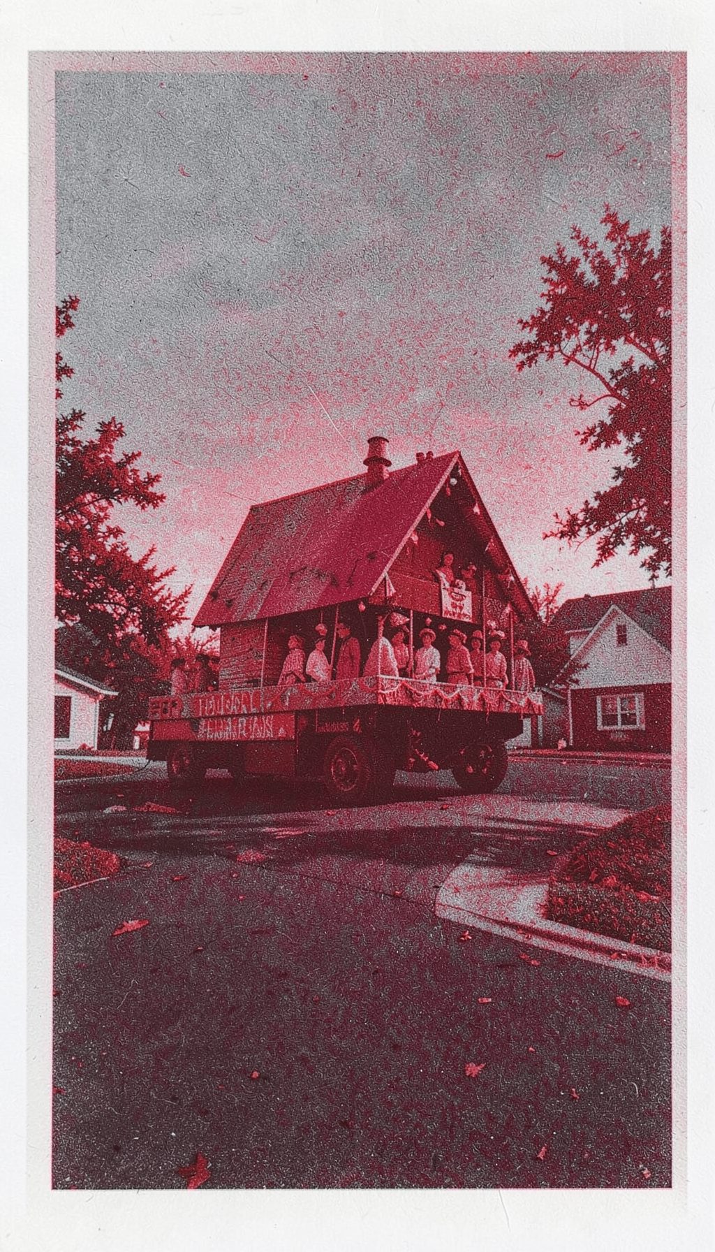 A two-ink risograph print in crimson and slate gray showing a Thanksgiving parade float looming ominously over a quiet suburban street at dusk.
